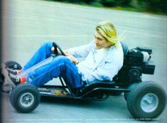 a woman sitting in a go kart with wheels on the street and smiling at the camera