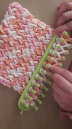 someone is holding a green and white comb with pink and white knitted material on it