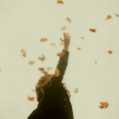 a woman reaching up into the air with her hands in the air and falling leaves