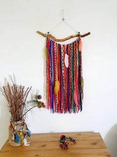 a wooden table topped with a vase filled with flowers and colorful tassels hanging from the wall