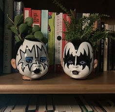 two painted faces are sitting on a shelf next to some books and planters with plants in them