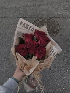 a person holding a bouquet of red roses on the street with newspaper paper wrapped around it