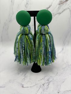 two green and blue tasselled earrings on a black stand with white marble background