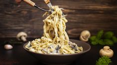 someone is eating pasta with mushrooms and parsley in a bowl on a wooden table