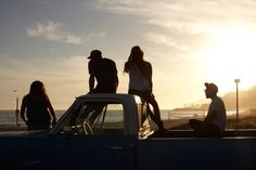 three people sitting on the back of a pick up truck in front of the ocean