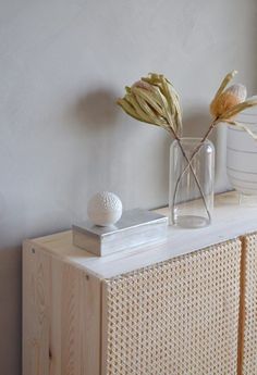 a vase filled with flowers sitting on top of a wooden cabinet next to a white wall