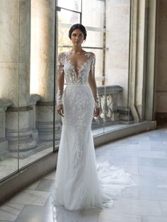 a woman in a white wedding dress standing by a glass wall and looking at the camera