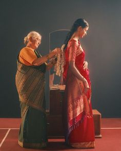 two women standing next to each other in front of a table with an object on it