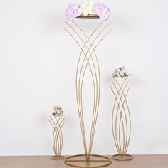 three metal flower vases with flowers in them sitting on a table next to a white wall