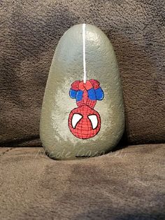 a rock with a spiderman painted on it sitting on top of a couch next to a pillow