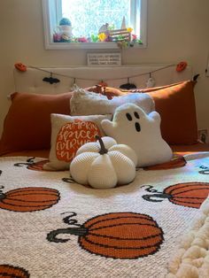 a bed topped with lots of pillows next to a window filled with pumpkins and ghost decorations