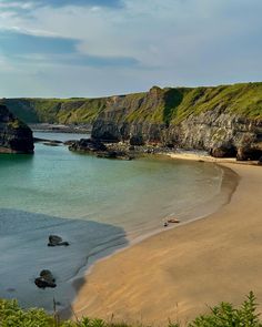 a sandy beach next to the ocean under a blue sky with green hills in the background