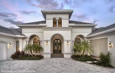 a large white house with lots of windows and palm trees in front of the entrance