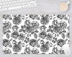 a computer mouse pad with black and white flowers on it next to a keyboard, coffee mug