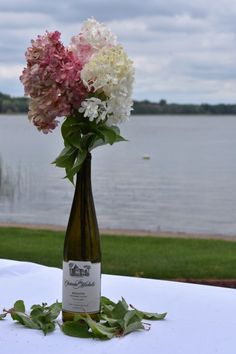 a bottle with flowers in it sitting on a table next to the water and grass