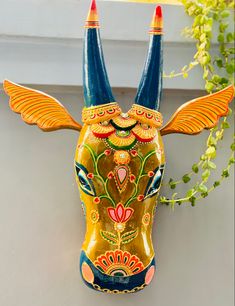 an animal mask with horns and wings painted on it's face is hanging from a wall