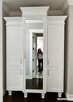 a woman standing in front of a large white closet with doors open and she is looking into the mirror