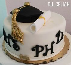 a white cake with black and gold decorations on it, topped with a graduation cap and tassel