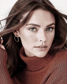 a beautiful woman with blue eyes wearing a brown turtle neck sweater and gold hoop earrings