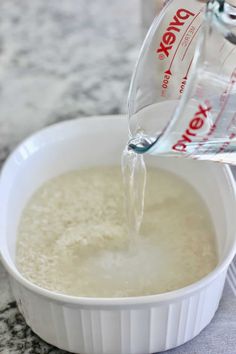 a pitcher pouring water into a white bowl filled with rice and other ingredients on a table