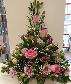 a vase filled with pink flowers on top of a white tablecloth covered floor next to a book shelf