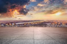 an empty concrete floor in front of a large cityscape with the sun going down