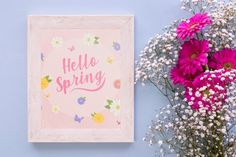 pink flowers are sitting next to a white frame with the words hello spring on it