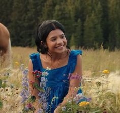 a woman in a blue dress sitting in a field with wildflowers and trees