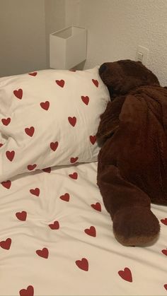 a teddy bear laying on top of a bed next to pillows with hearts all over it