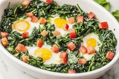 eggs and spinach in a white bowl on a marble countertop next to lettuce