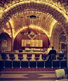 the inside of a bar with chairs and lights on it's walls, along with an arched brick ceiling