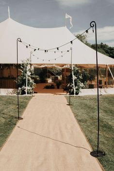 an outdoor ceremony with white tents and string lights on the walkway leading up to the tent