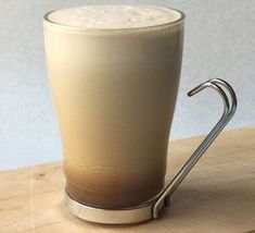 a tall glass with liquid in it sitting on top of a wooden table next to a metal handle