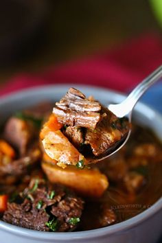 a spoonful of beef stew with carrots and parsley in a white bowl