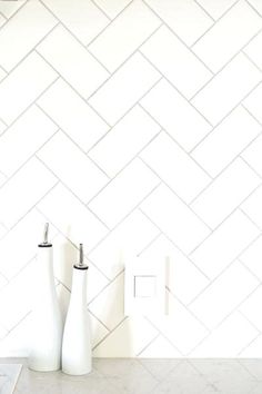 three white vases sitting on top of a counter in front of a tiled wall