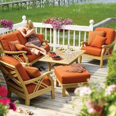 a woman sitting on a wooden deck with orange chairs and an ottoman in front of her