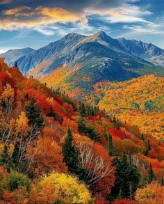 the mountains are covered in colorful trees and foliage, as well as clouds above them