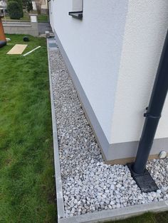 the side of a building with rocks and grass around it, next to a black pipe