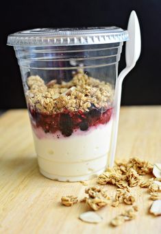 a cup filled with yogurt and granola on top of a wooden table