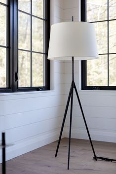 the floor lamp is in front of two windows with black frames and white lampshades