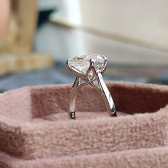 a diamond ring sitting on top of a pink velvet holder with a white background and blurry image in the background