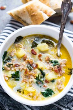 a bowl of soup with spinach, sausage and bread on the side next to it