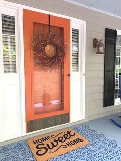 an orange door with a welcome mat in front of it