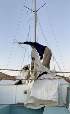 a man is standing on top of a sailboat with his hands in the air