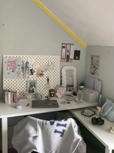 a cluttered desk in an attic with pictures on the wall and other items around it