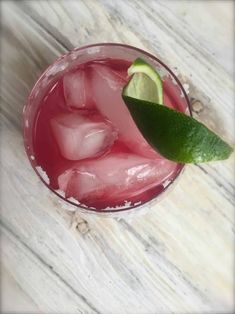 a close up of a drink with ice and a lime on the rim, sitting on a wooden table