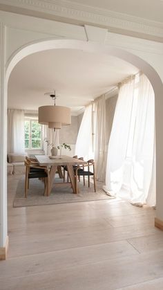 an archway leading into a dining room with white curtains and table in the center,