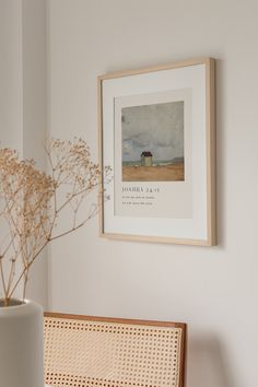 a white vase with some flowers in it next to a framed photo on the wall