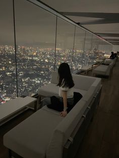 a woman sitting on top of a white bench in front of a cityscape