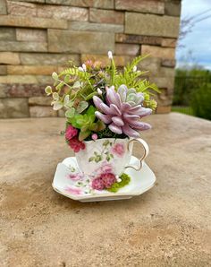 a tea cup with flowers in it sitting on a stone table next to a brick wall